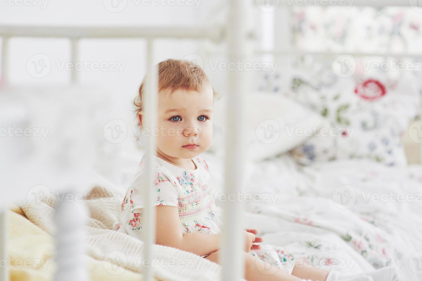 conceito de infância. menina com vestido bonito localização na cama brincando com brinquedos em casa. quarto infantil branco vintage foto