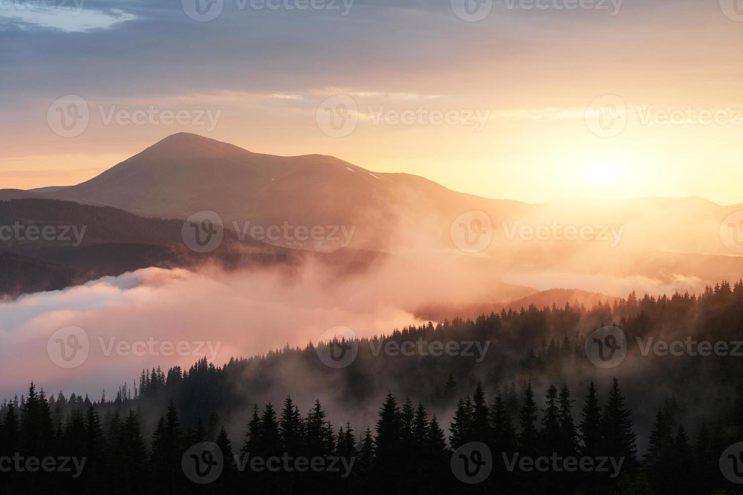 belo pôr do sol nas montanhas. paisagem com a luz do sol brilhando através de nuvens laranja e neblina foto