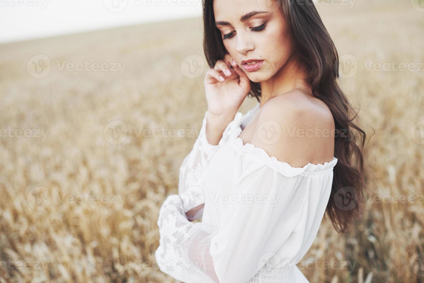 jovem sensível em um vestido branco posando em um campo de trigo dourado foto