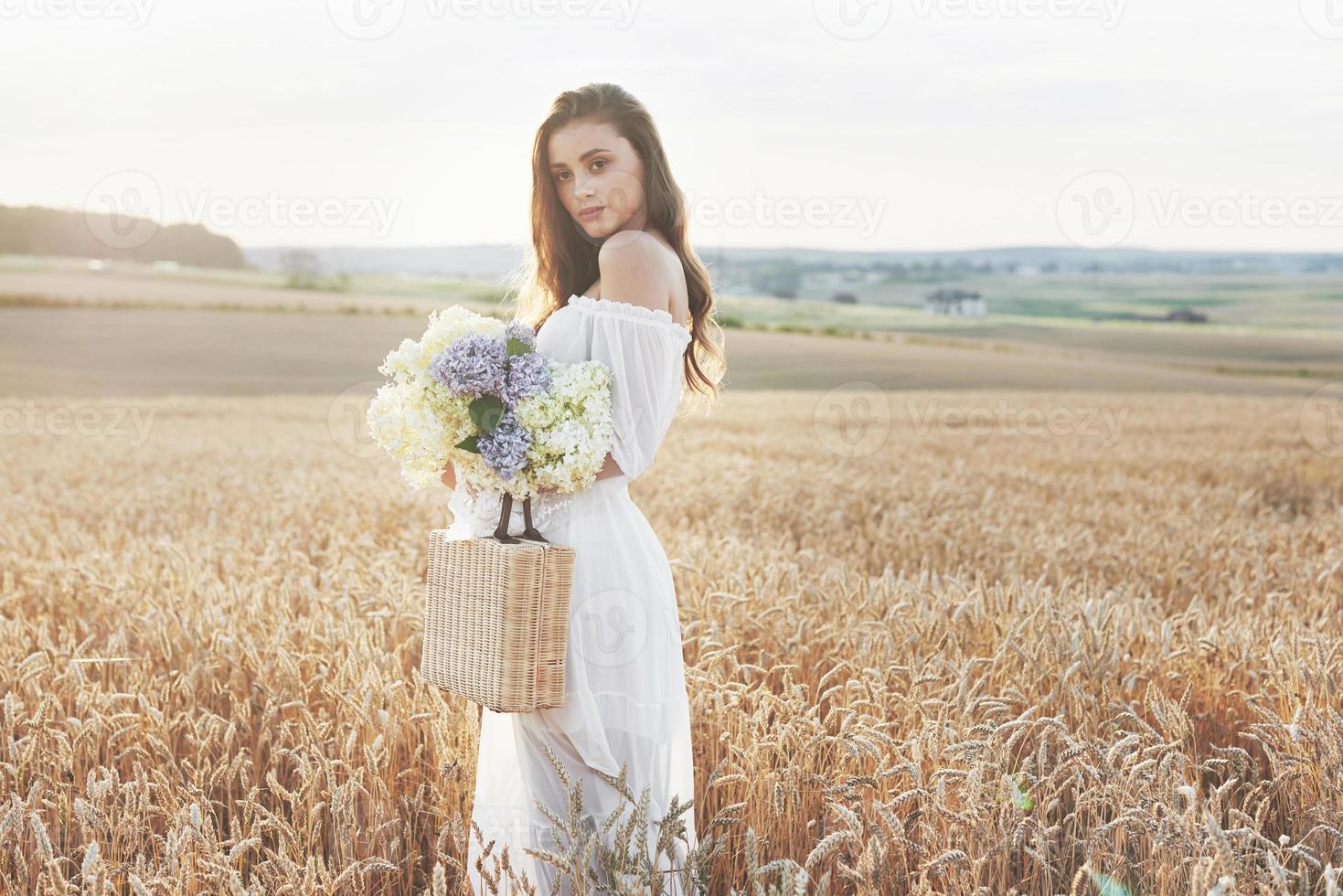 linda garota de vestido branco correndo no campo de trigo de outono ao pôr do sol foto