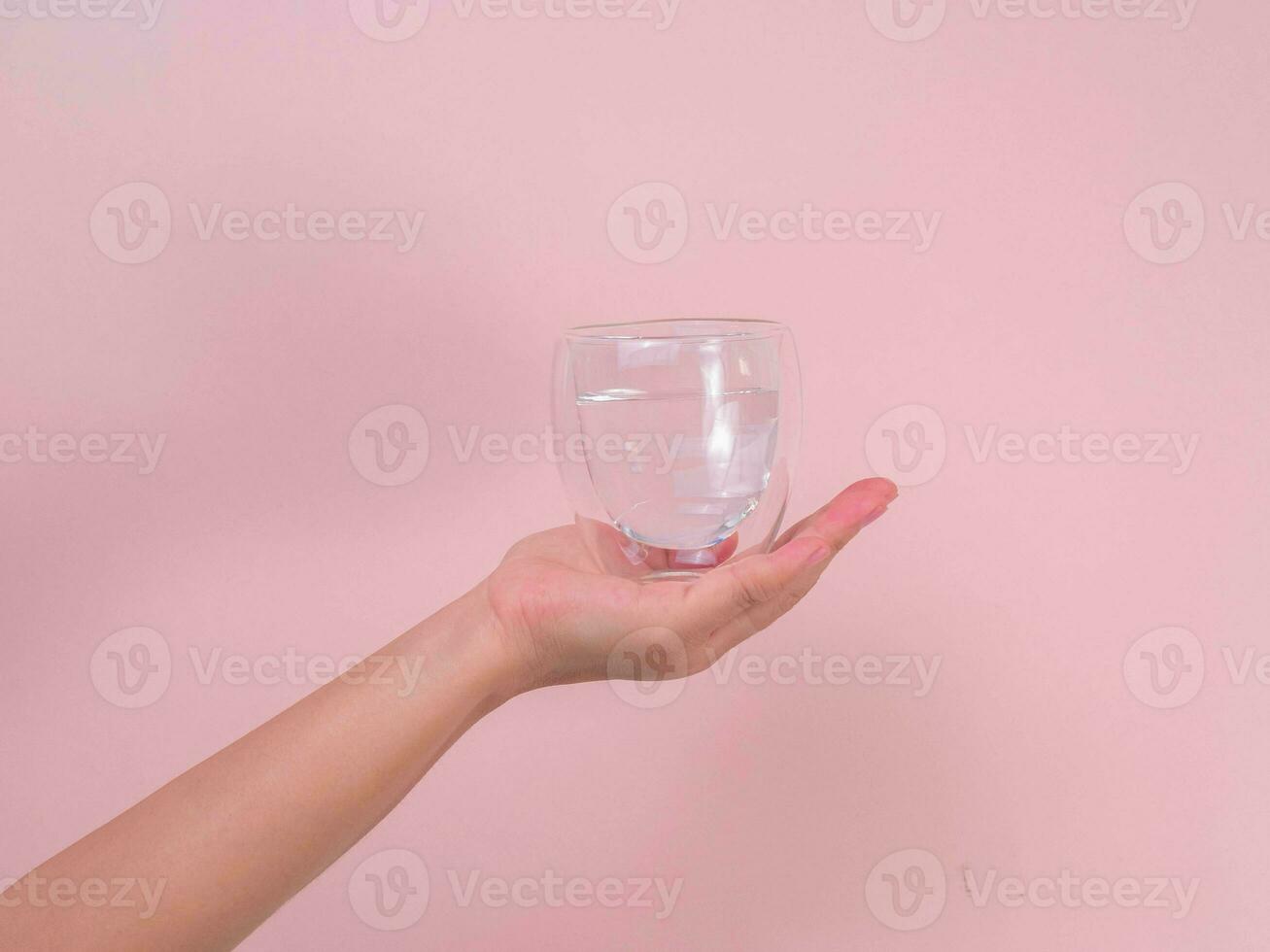 fêmea mão segurando vidro do água isolado em Rosa fundo. foto