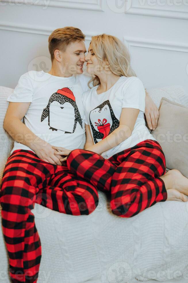 alegre e feliz casal dentro Coincidindo pijamas deitado em sofá. uma amoroso família. a conceito do Novo anos feriados foto