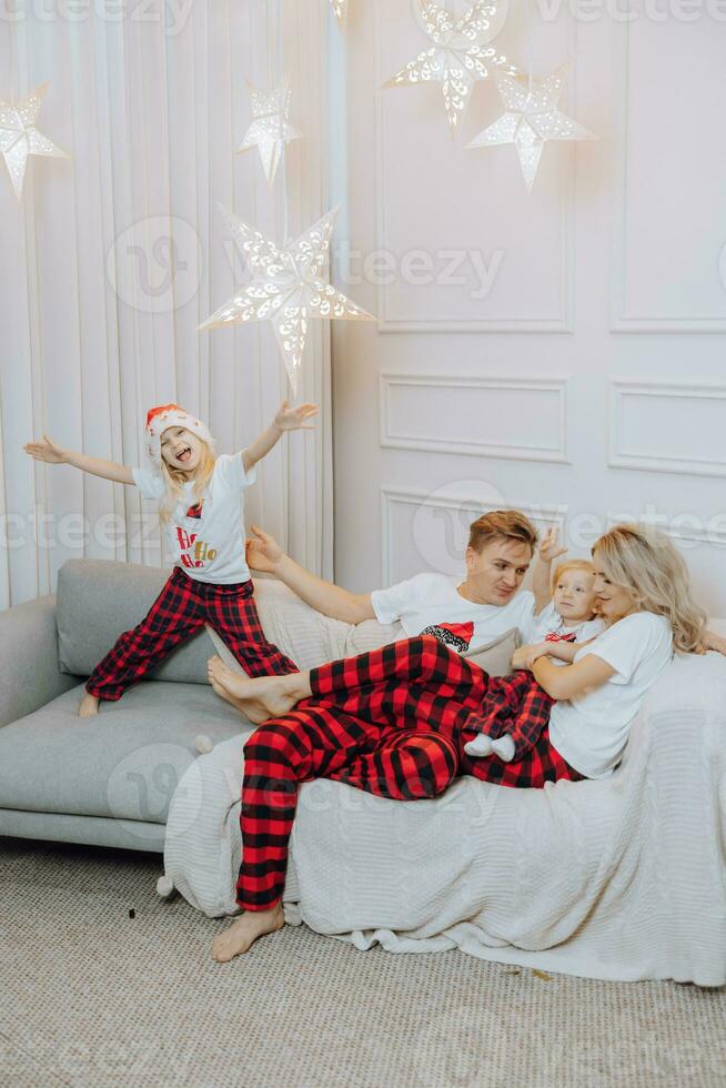 alegre e feliz família dentro idêntico pijamas deitado em a sofá. crianças estão tendo Diversão. amoroso família com presentes dentro a sala. foto