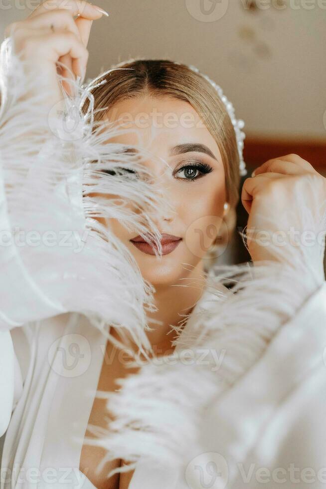 retrato do uma lindo noiva dentro uma hotel dentro a elegante branco roupão com Largo mangas. preparação para a Casamento cerimônia. foto