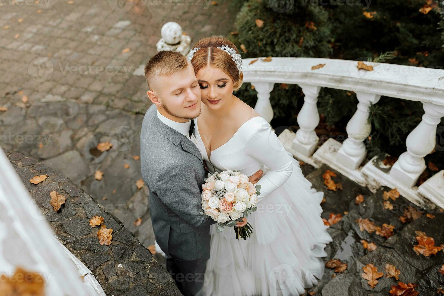 retrato do a noiva e noivo a partir de acima. a noiva dentro uma Casamento vestir em a elegante Escadaria. noivo dentro uma clássico cinzento terno, branco camisa e arco gravata. ele leva isto ausente. Casamento dentro uma topo localização foto