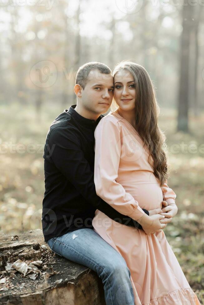 uma homem e dele grávida esposa abraço e beijo dentro a floresta às pôr do sol. feliz família conceito. foto