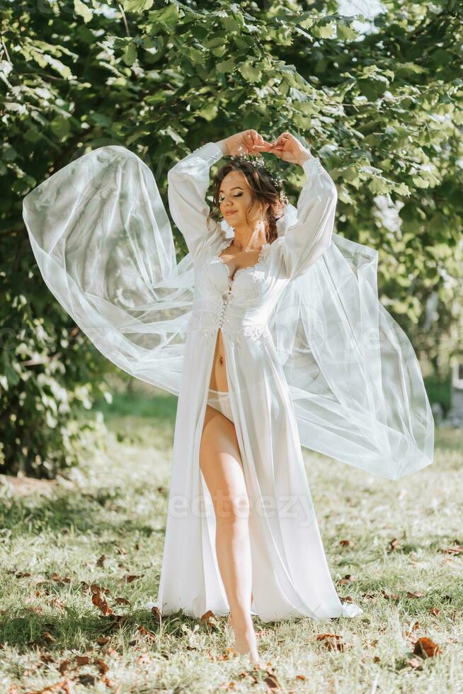 retrato do uma sonhadores noiva em pé dentro uma jardim. a lindo noiva é vestido dentro uma branco roupão e uma tiara do fresco flores em dela cabeça. foto