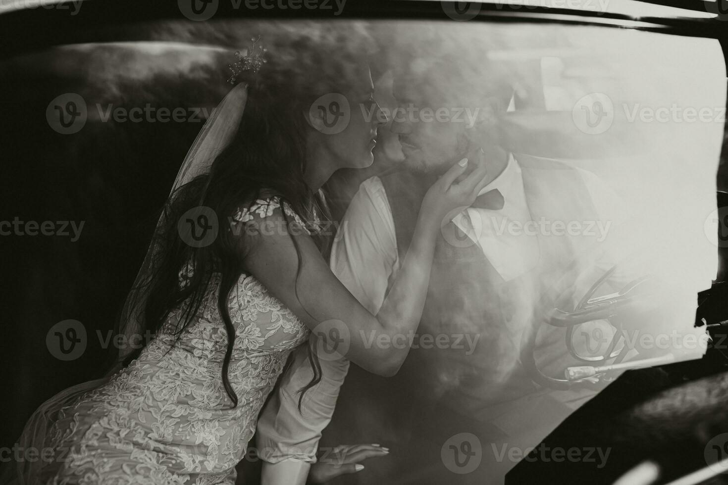 uma luxuoso e elegante Casamento casal ternamente abraço dentro a meio do uma à moda retro carro. a foto estava ocupado através a parabrisa. linda noiva e bonito noivo dentro retro estilo.