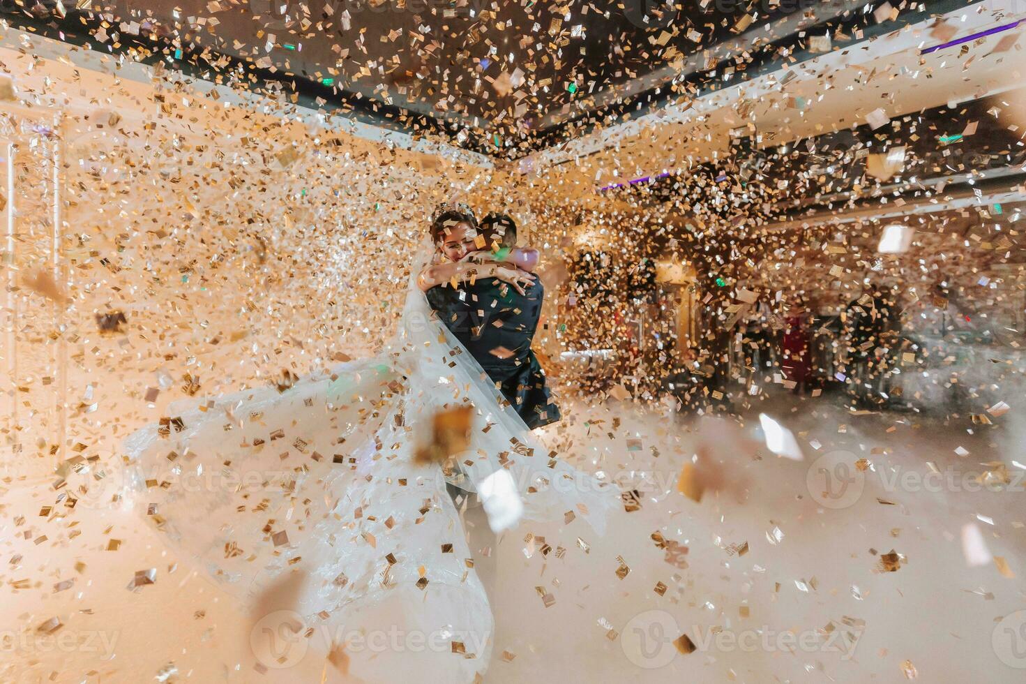 linda noiva e à moda noivo dançando debaixo dourado confete às Casamento recepção. feliz Casamento casal realizando primeiro dança dentro restaurante. romântico momentos foto