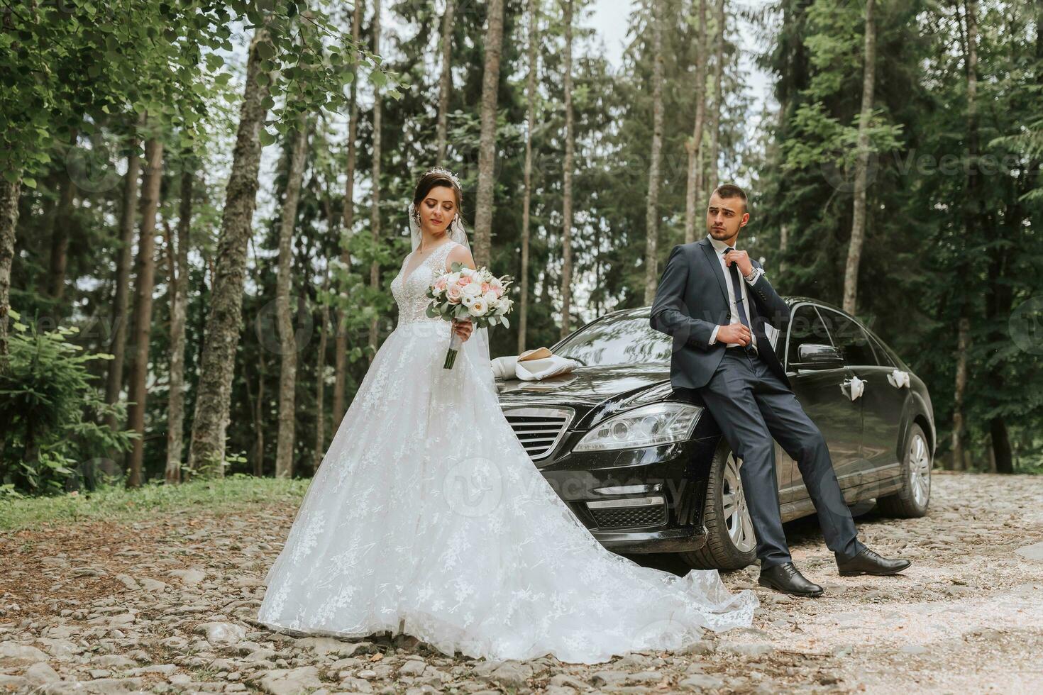 frente Visão do uma casado noiva e noivo vestindo festivo roupas em pé contra uma Preto carro em seus Casamento dia foto