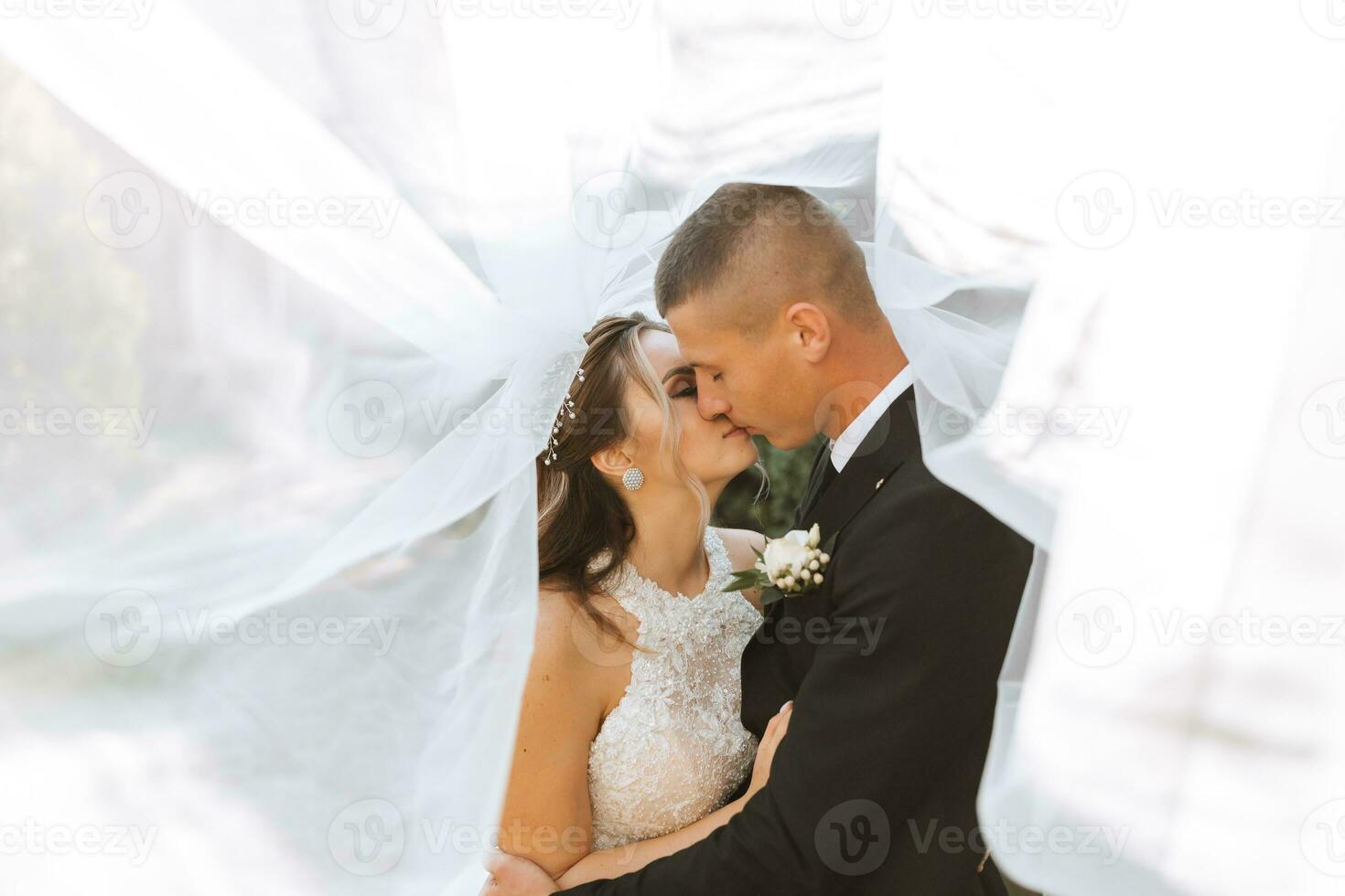 linda feliz luxuoso morena noiva e elegante à moda noivo ficar de pé debaixo uma véu e abraço ternamente foto