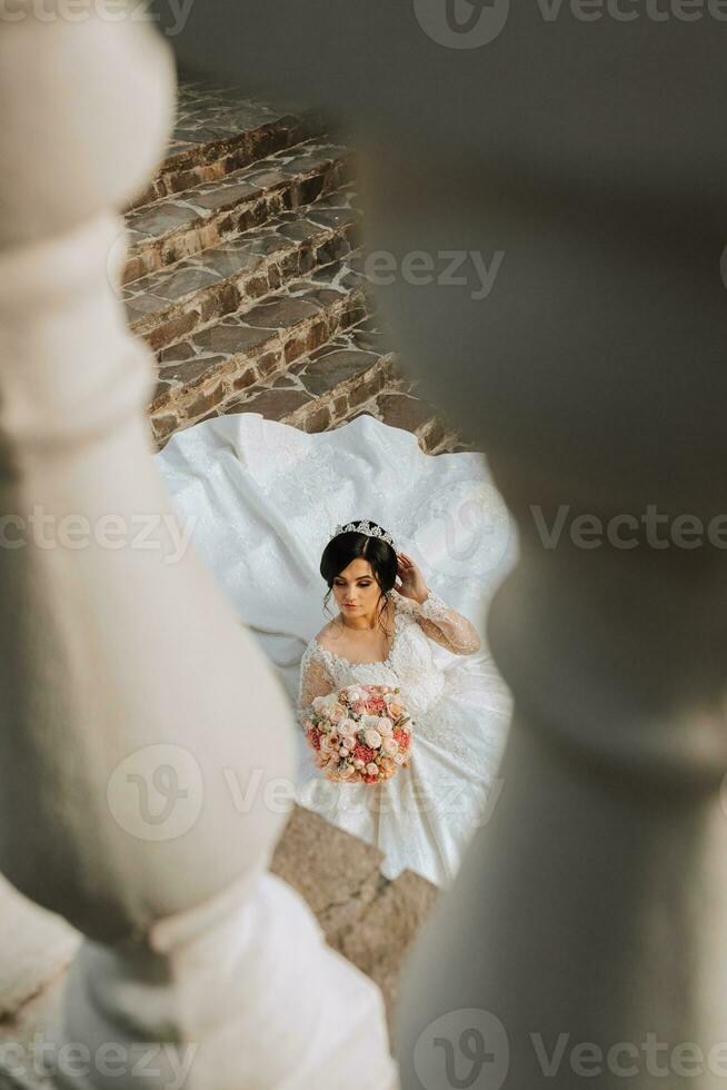 jovem lindo noiva dentro Casamento vestir e coroa em cabeça deitado em pedra passos, moda tiro debaixo severo luz solar. a foto é ocupado a partir de acima