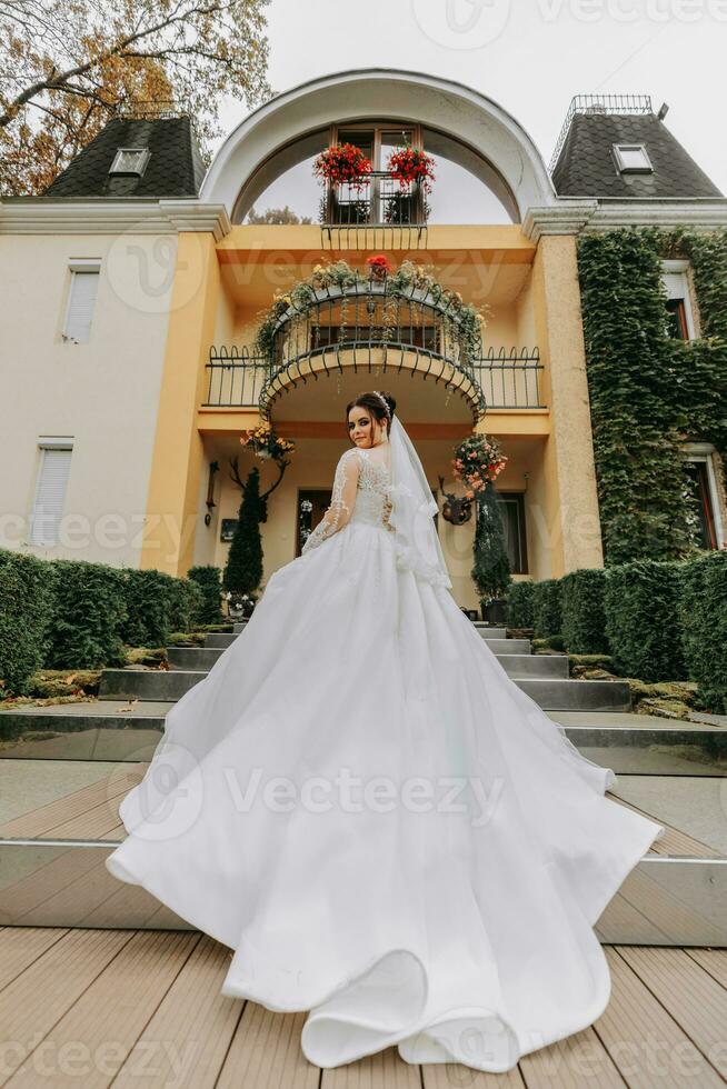 linda noiva dentro Casamento vestir com grandes trem e véu ao ar livre. a noiva contra a fundo do a caro hotel foto