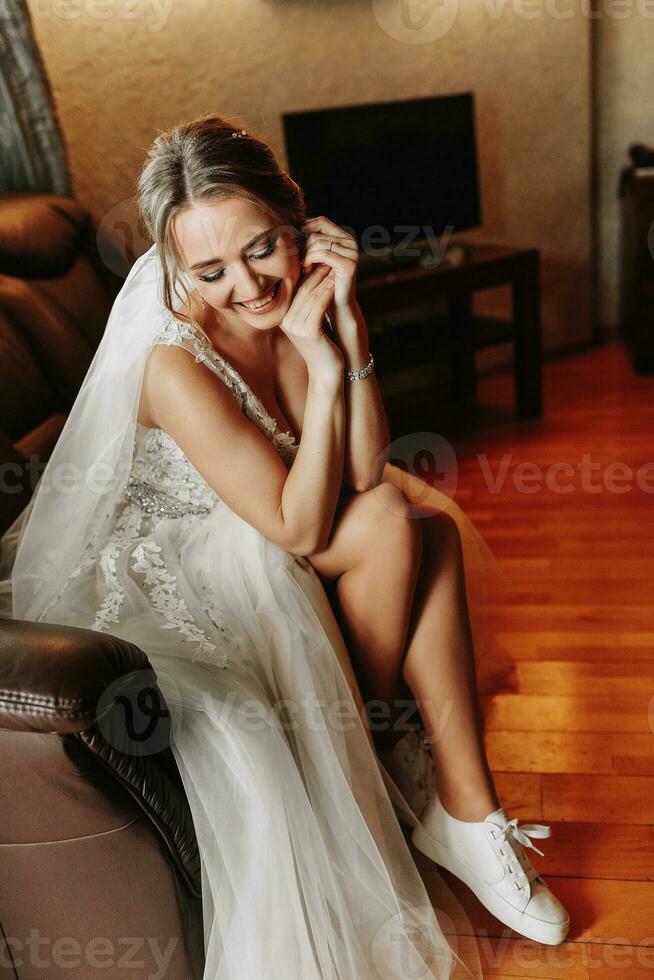 a feliz noiva colocar em tênis. preparando a noiva para a cerimônia. confortável sapatos para uma casamento. branco tênis. nu joelhos. foto