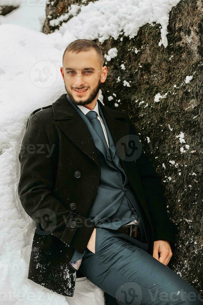 bonito confiante jovem barbudo homem em pé dentro Nevado quintal, elegante homem vestindo caro roupas posando ao ar livre foto