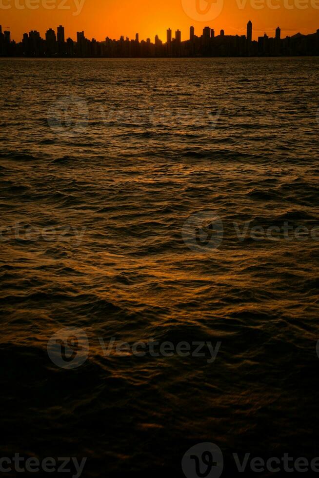 pôr do sol dentro a meio do a mar e silhueta do a cidade foto