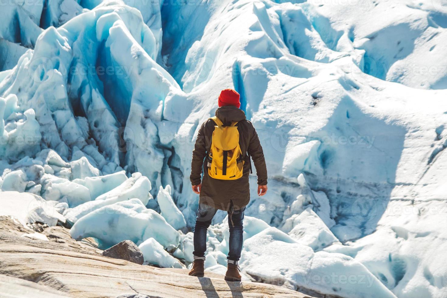 homem viajante de pé sobre uma rocha no fundo de uma geleira, montanhas e neve foto