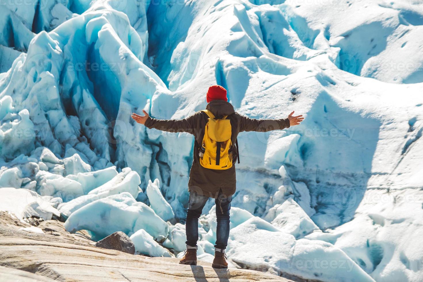 homem com mochila em pé sobre uma rocha no fundo de uma geleira e neve foto