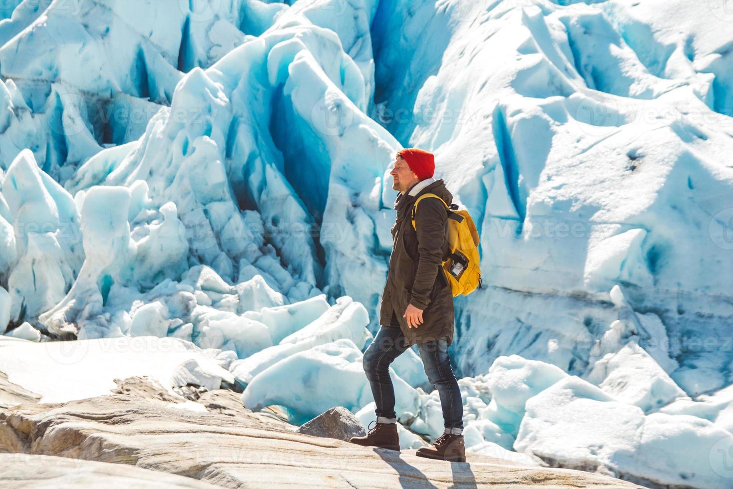 homem com mochila em pé sobre uma rocha no fundo de uma geleira e neve foto