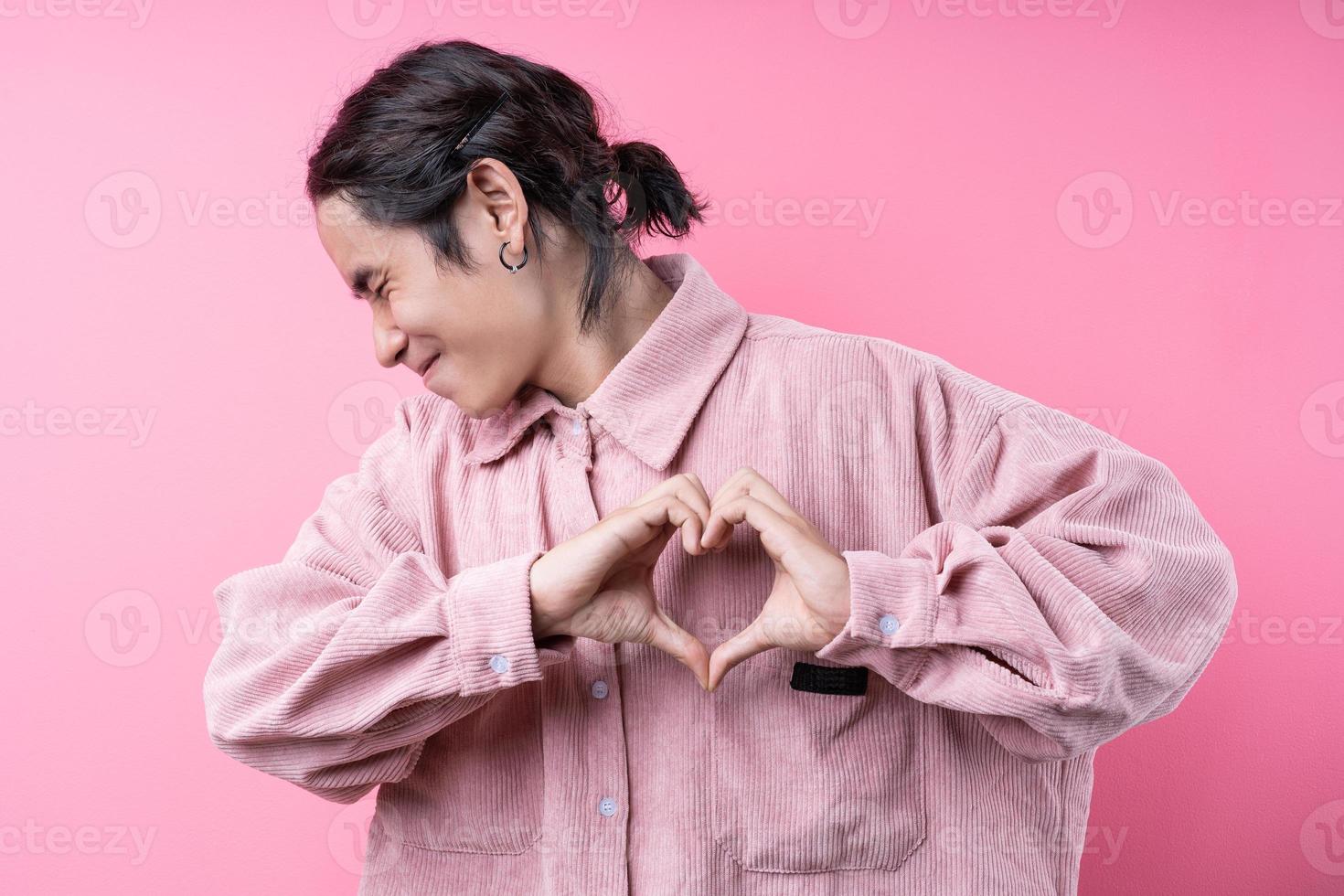 jovem asiático de cabelos compridos, vestindo uma camisa rosa, sorrindo no fundo rosa foto