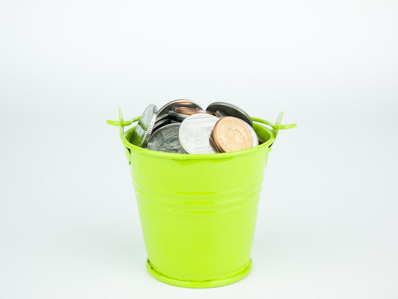 moedas de dinheiro em balde verde sobre fundo branco, conceito de negócio foto
