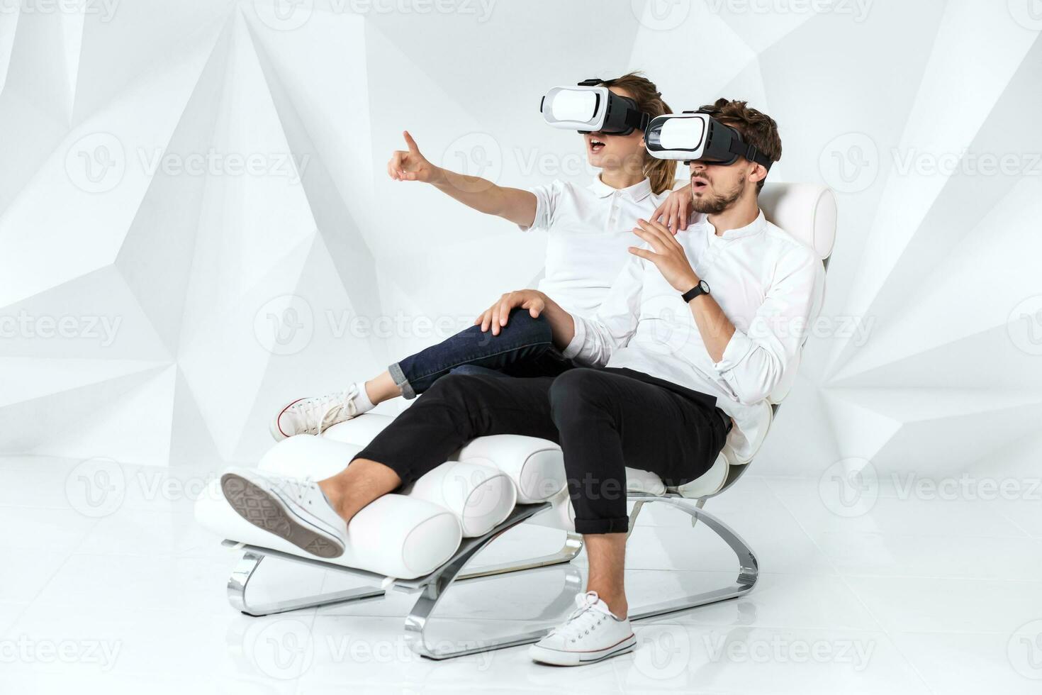 uma jovem casal vestindo vr fones de ouvido sentado em branco cadeira dentro uma quarto com branco paredes e pavimentos foto