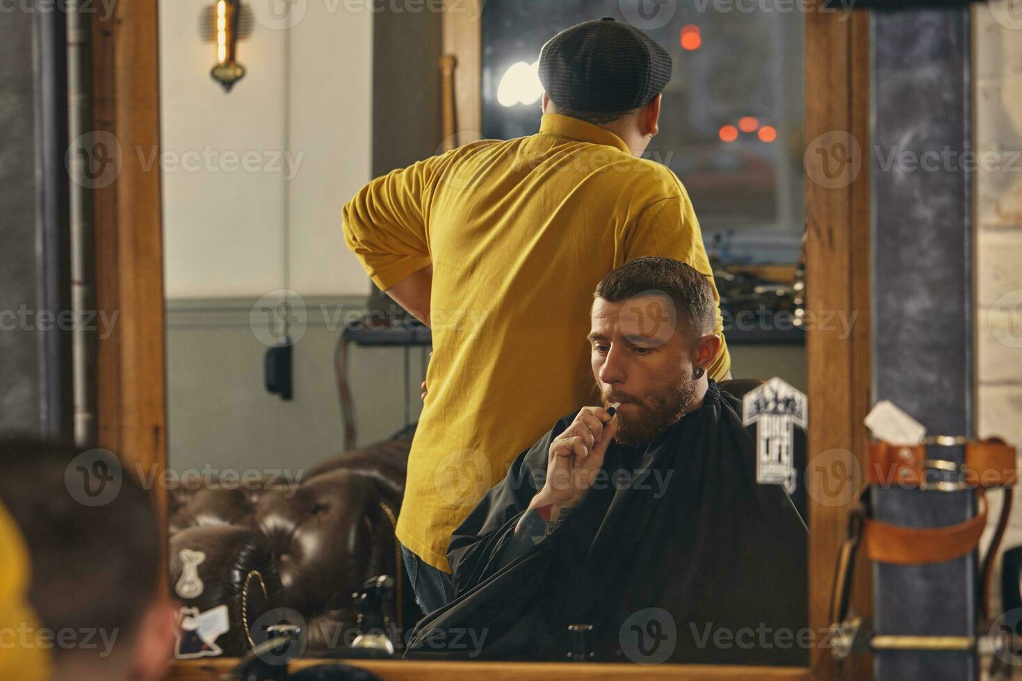 barbeiro fazendo corte de cabelo de atraente homem barbudo na barbearia foto