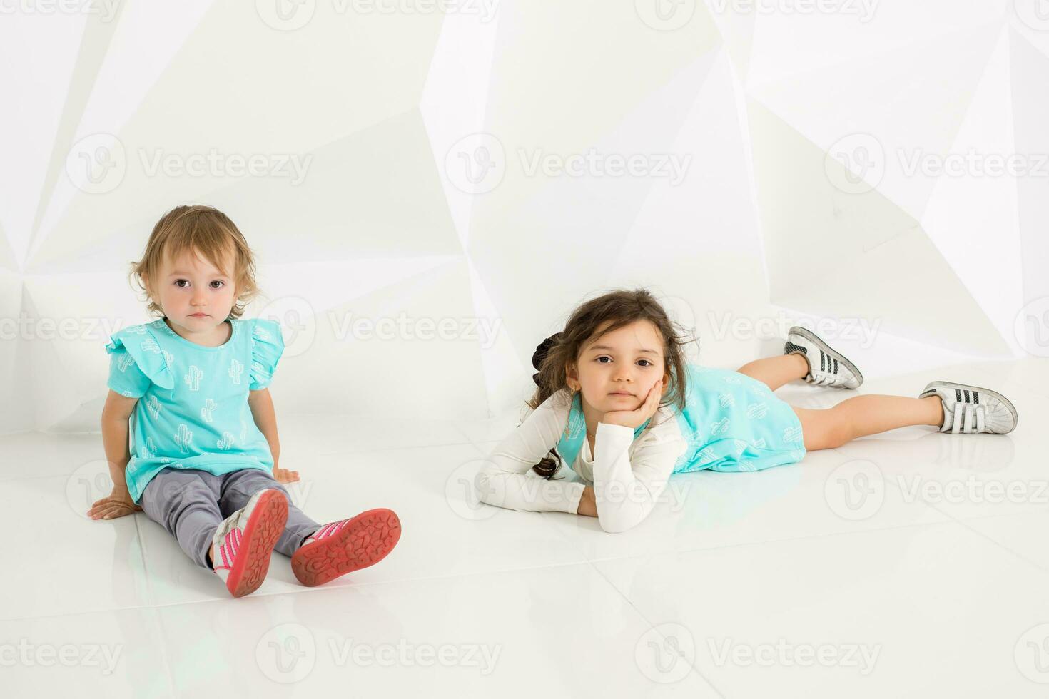 dois fofa pequeno meninas em pé dentro turquesa vestem em a branco parede fundo dentro a estúdio. foto