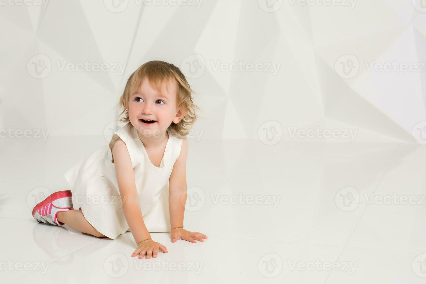sorridente pequeno menina sentado em a chão em uma branco fundo foto