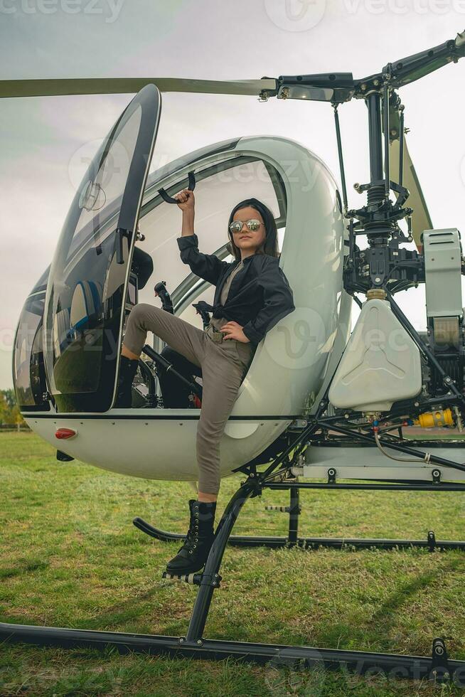 confiante pré-adolescente menina dentro espelhado oculos de sol em pé em estribo do helicóptero foto