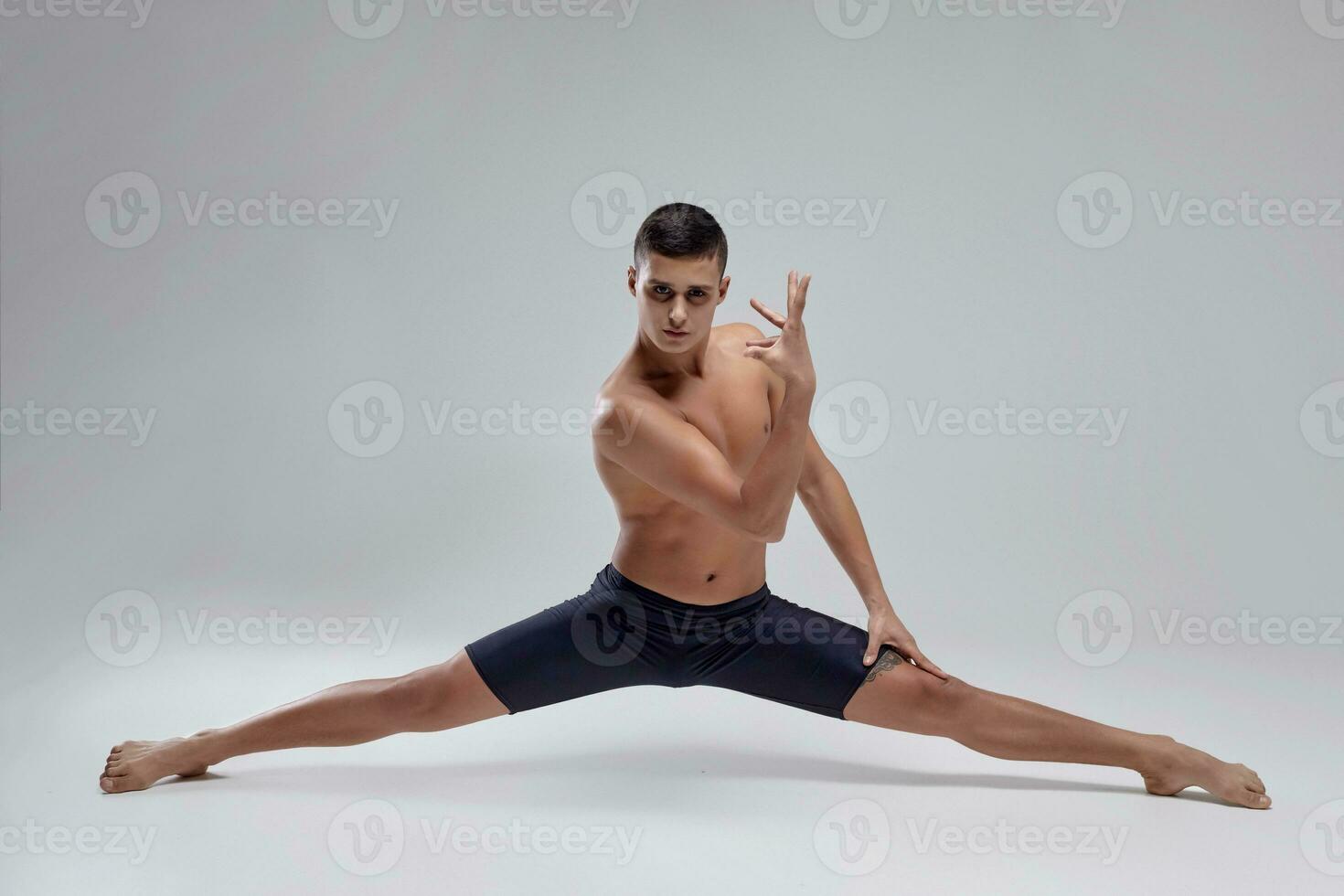 foto do uma bonito homem balé dançarino, vestido dentro uma Preto shorts, fazer uma dança elemento contra uma cinzento fundo dentro estúdio.