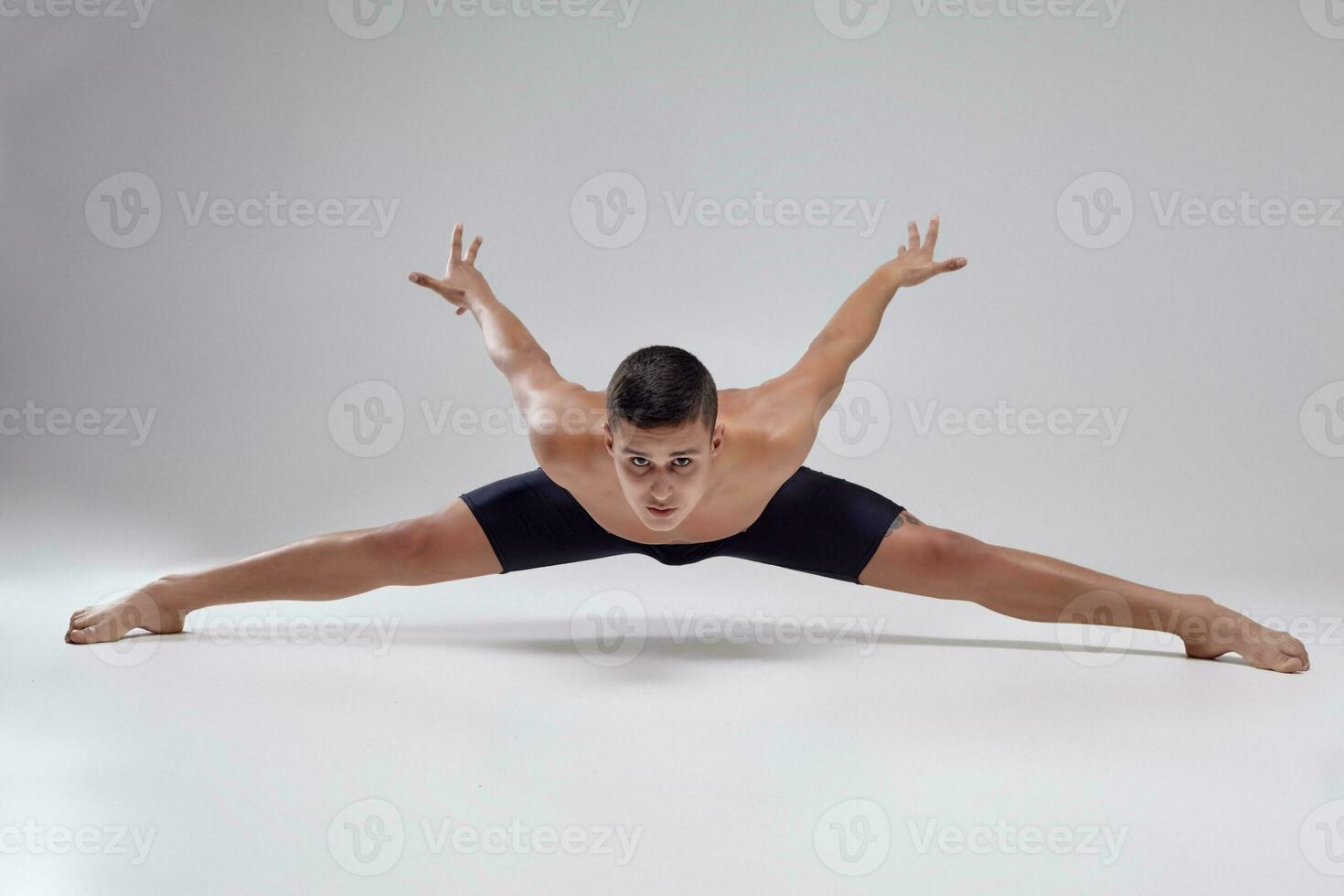 foto do uma bonito homem balé dançarino, vestido dentro uma Preto shorts, fazer uma dança elemento contra uma cinzento fundo dentro estúdio.