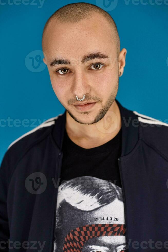 estúdio tiro do uma jovem tatuado Careca homem posando contra uma azul fundo. anos 90 estilo. foto