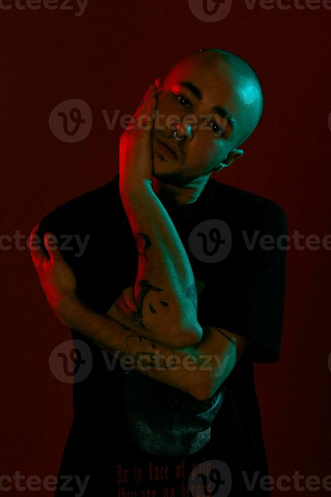 estúdio tiro do uma jovem tatuado Careca homem posando contra uma vermelho fundo. anos 90 estilo. foto