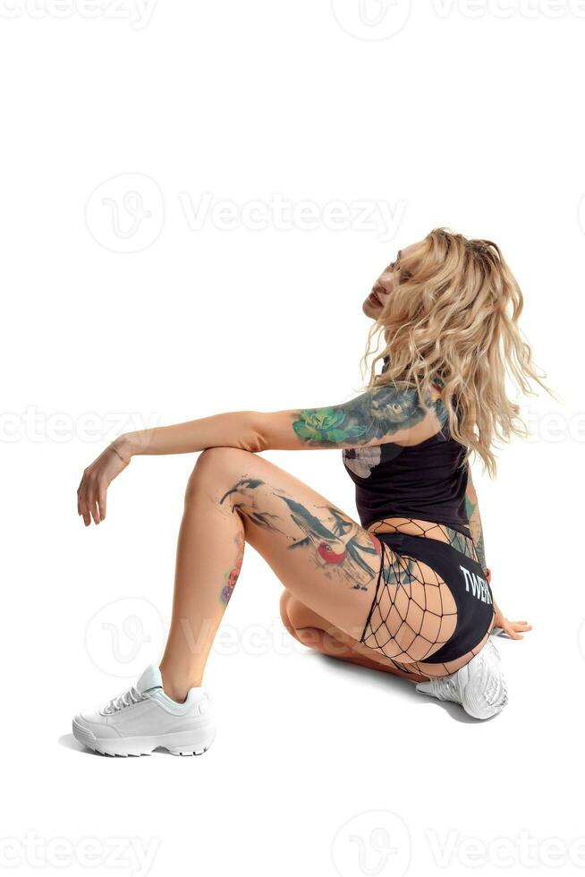 sexy loiro rebolar mulher com tatuado corpo e grandes encaracolado cabelo é posando dentro estúdio. foto