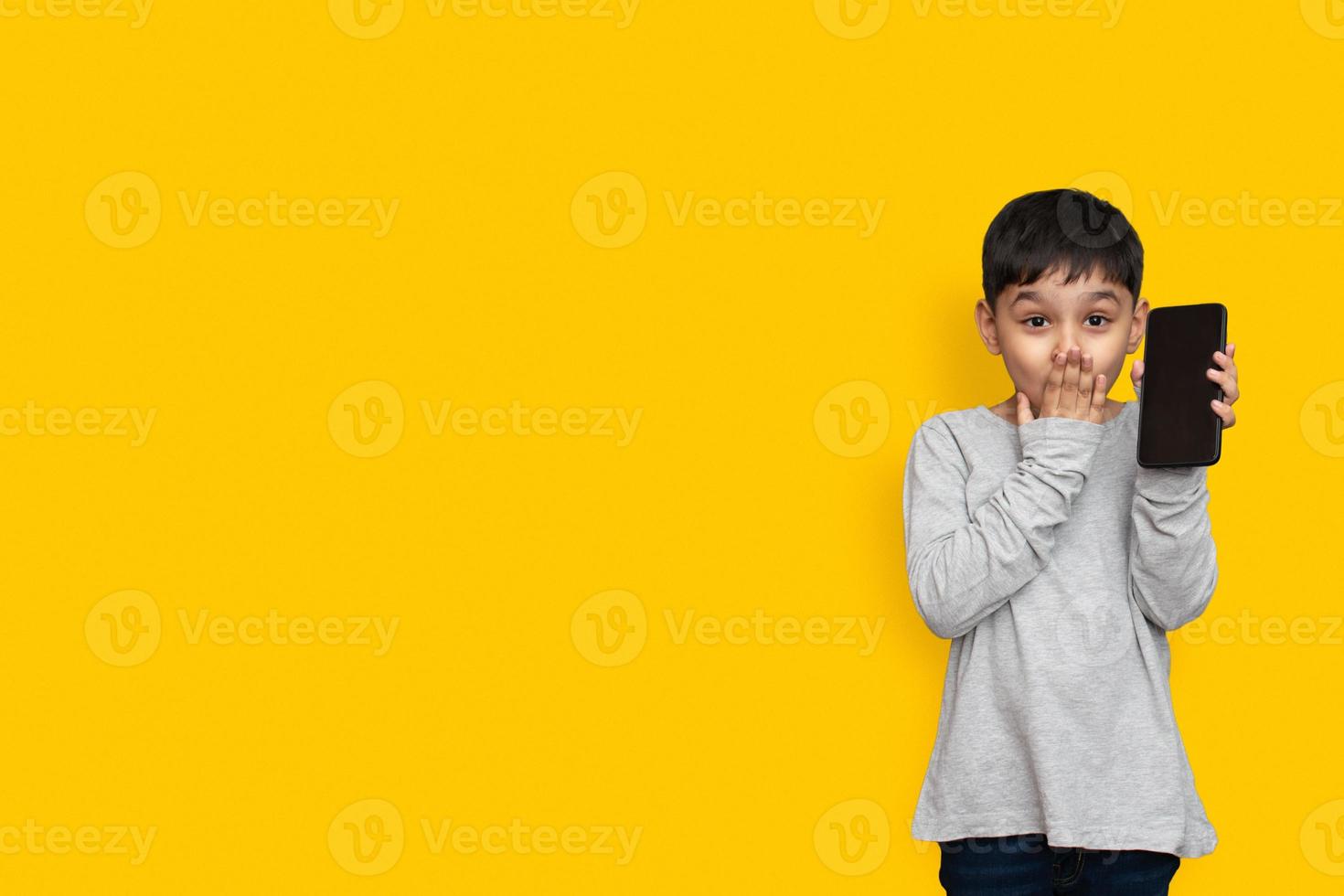 sorrir e chocar o garotinho na tela em branco da camisa verde cinza do telefone móvel no espaço de cópia de fundo amarelo foto