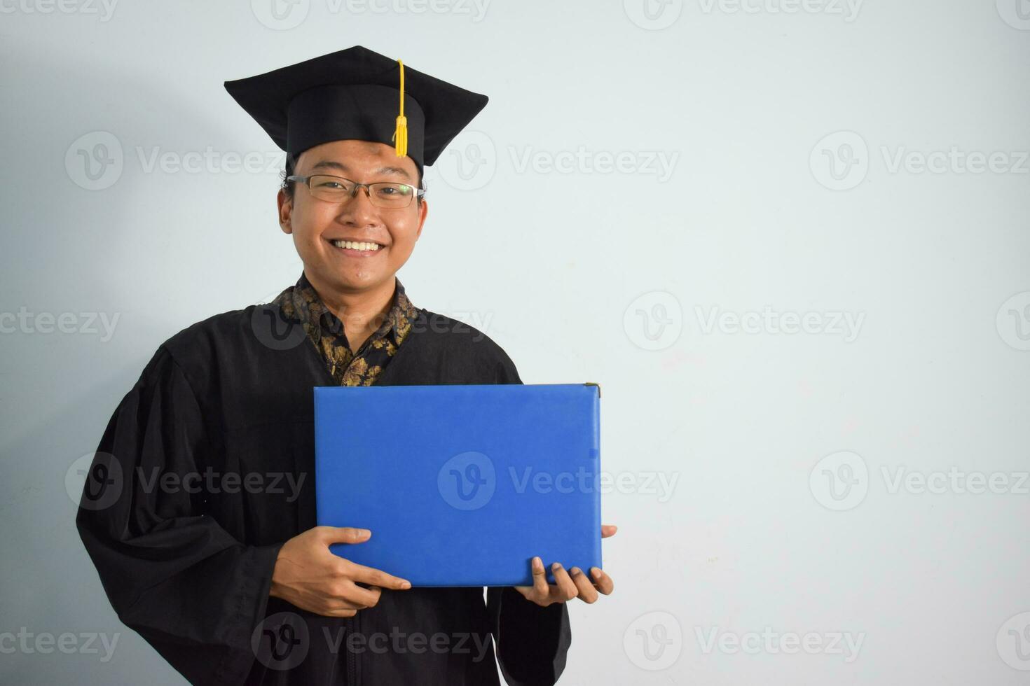 expressivo do adulto Indonésia masculino vestem graduação manto, chapéu e Óculos, ásia masculino graduação trazer em branco azul certificado isolado em branco fundo, expressões do retrato graduação foto