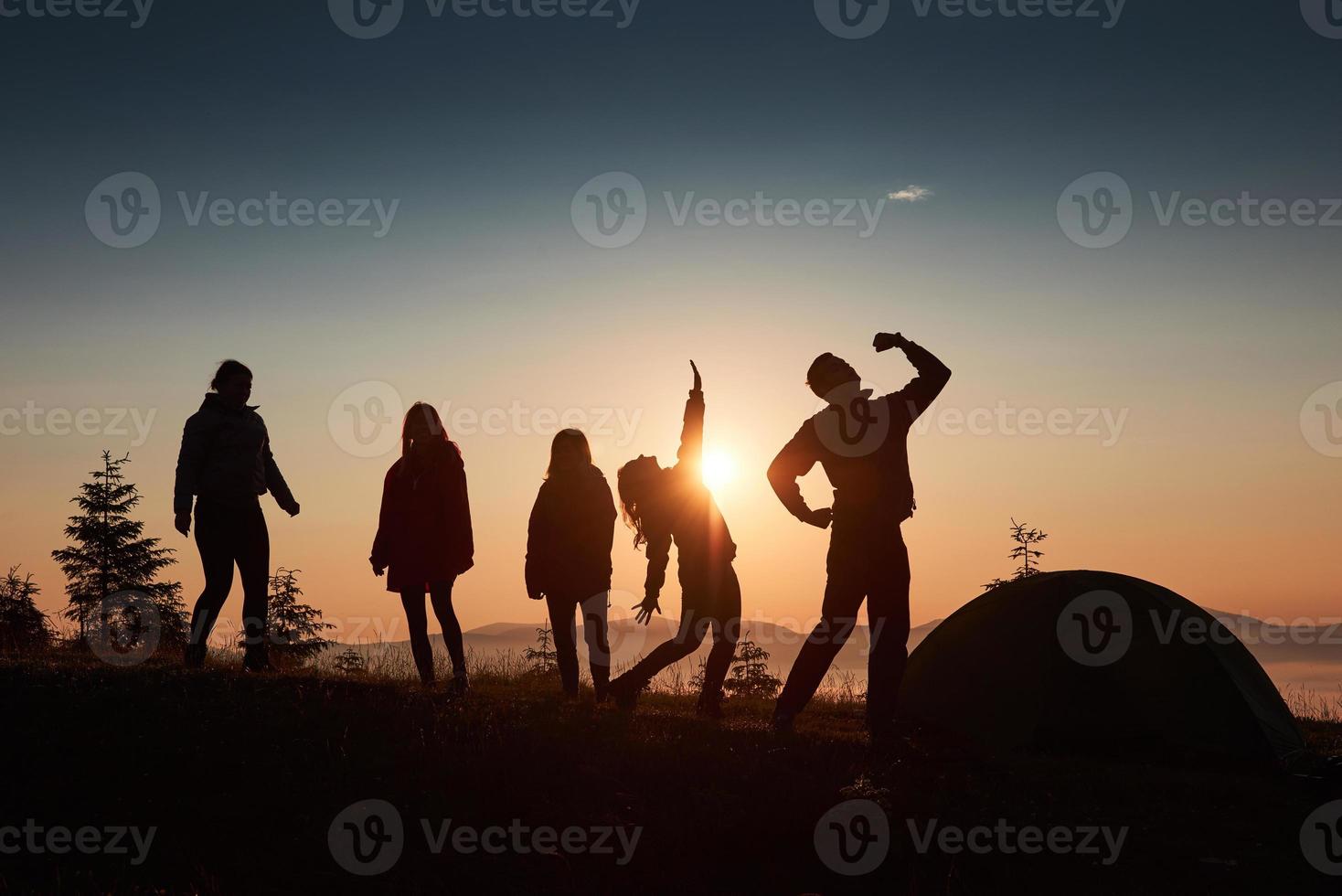 uma silhueta de um grupo de pessoas se divertindo no topo da montanha perto da barraca durante o pôr do sol foto