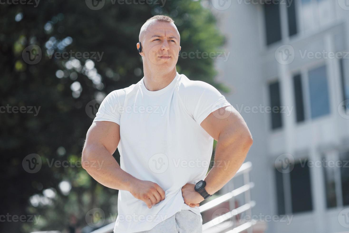 um homem bonito de fitness em uma roupa esportiva, fazendo alongamento enquanto se prepara para exercícios sérios na cidade moderna foto