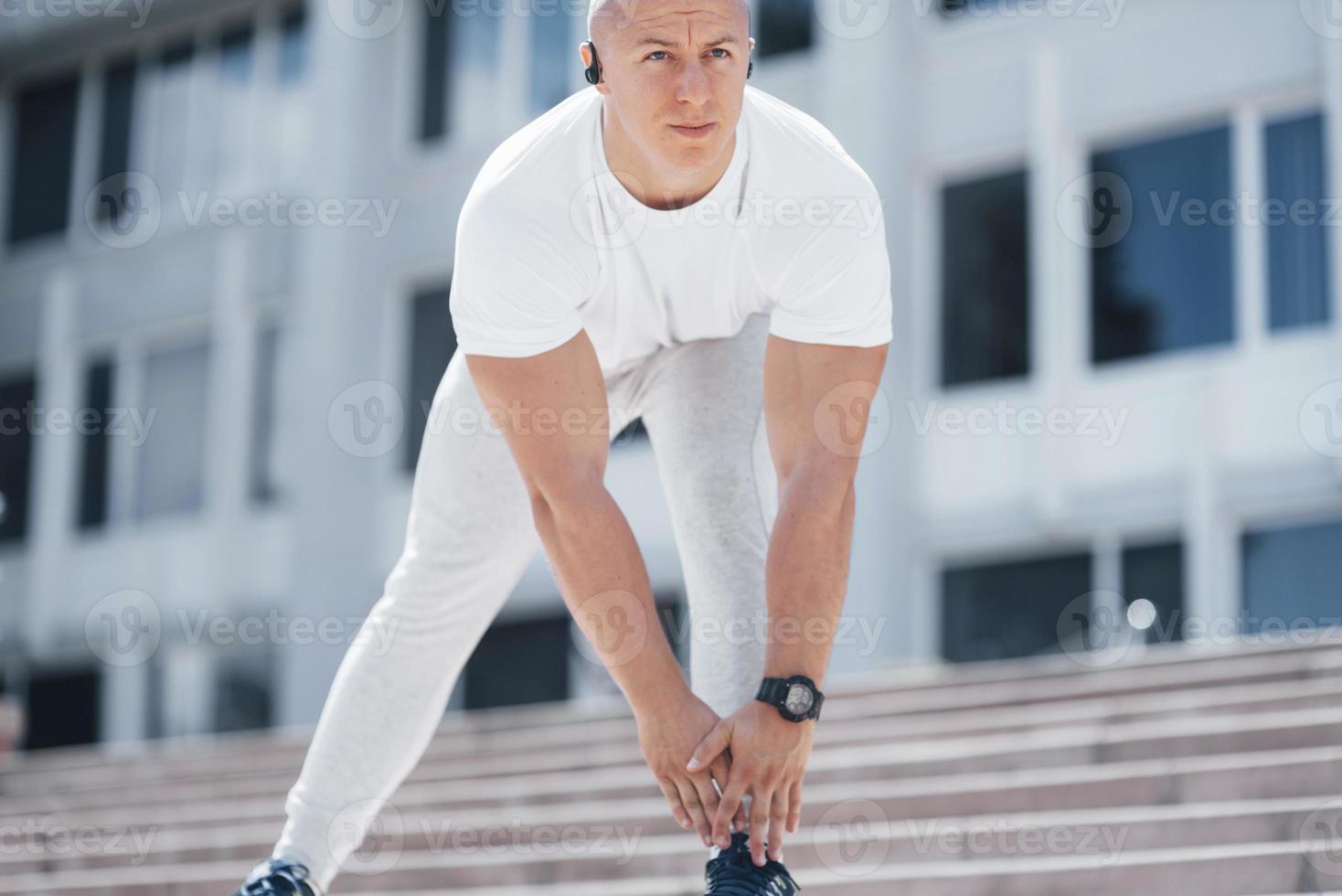 um homem bonito de fitness em uma roupa esportiva, fazendo alongamento enquanto se prepara para exercícios sérios na cidade moderna foto