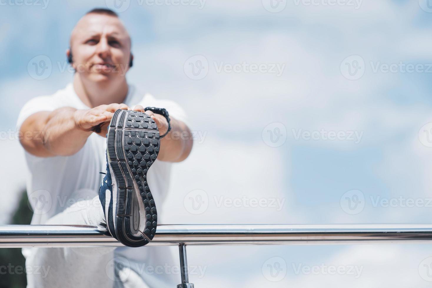 um homem bonito de fitness em uma roupa esportiva, fazendo alongamento enquanto se prepara para exercícios sérios na cidade moderna foto