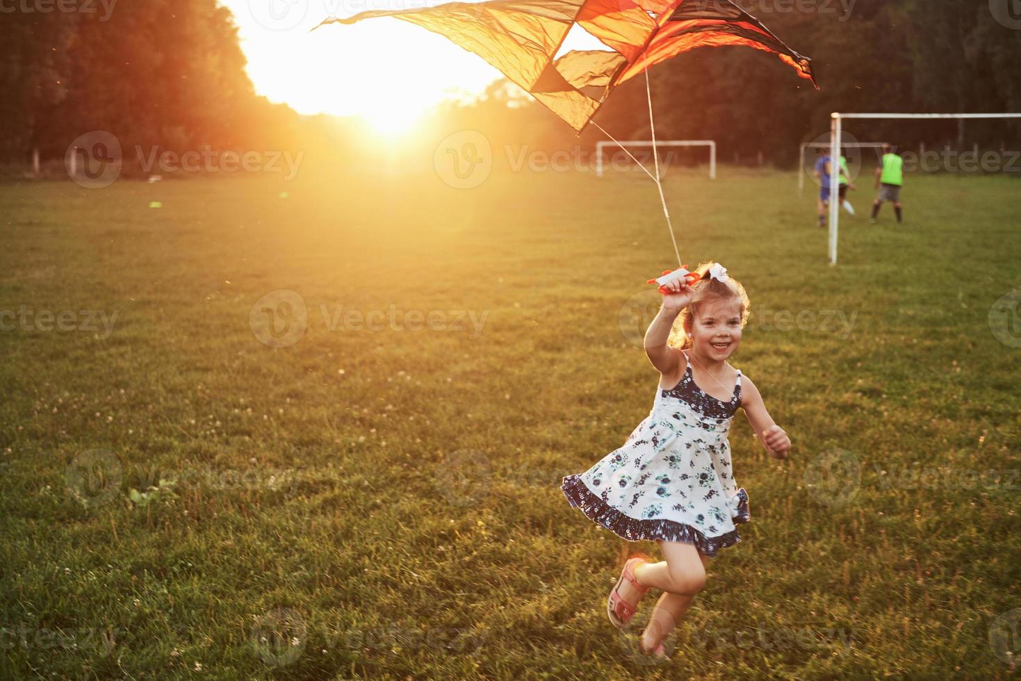 menina bonitinha com cabelo comprido correndo com a pipa no campo em um dia ensolarado de verão foto