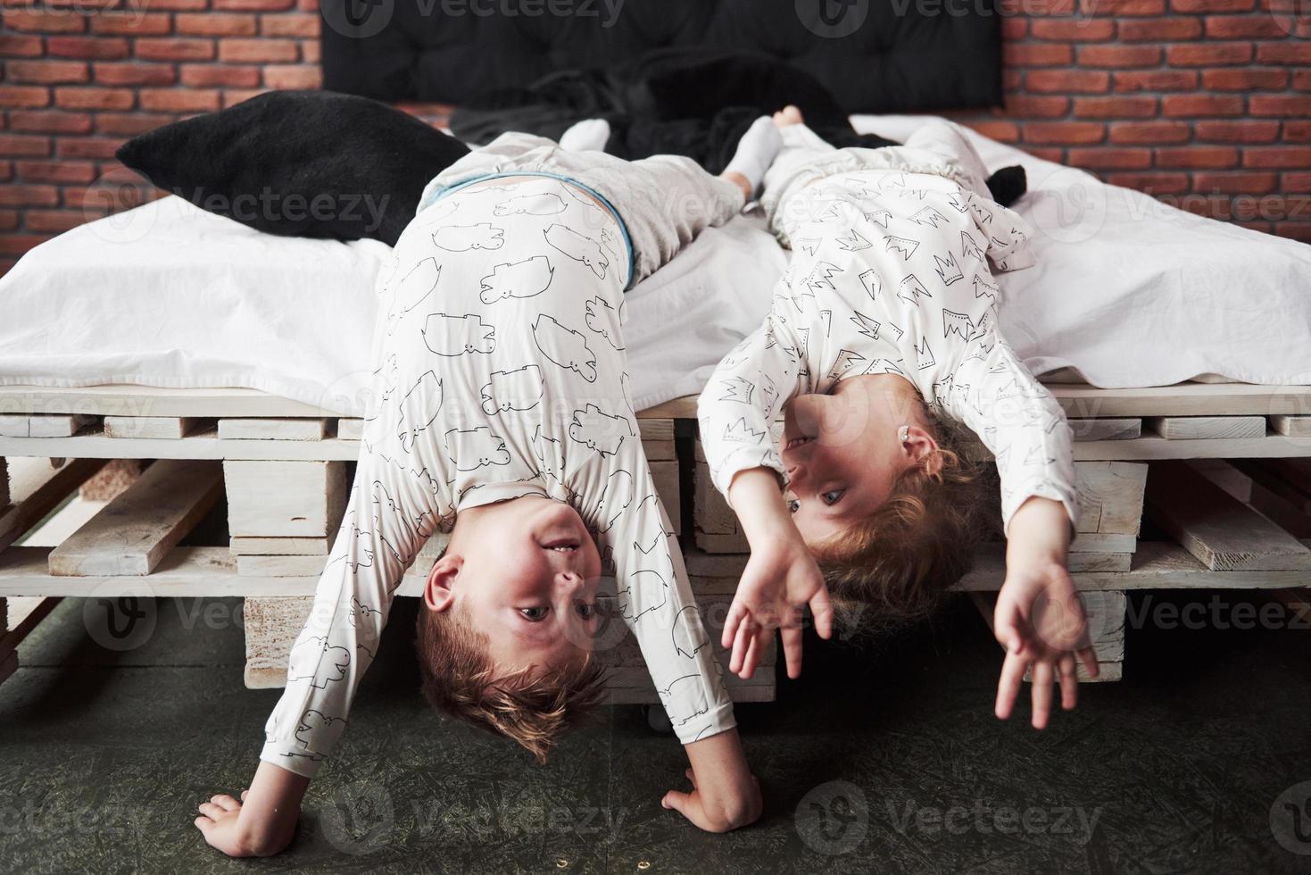 crianças felizes brincando no quarto preto. menino e menina, irmão e irmã brincam na cama de pijama foto