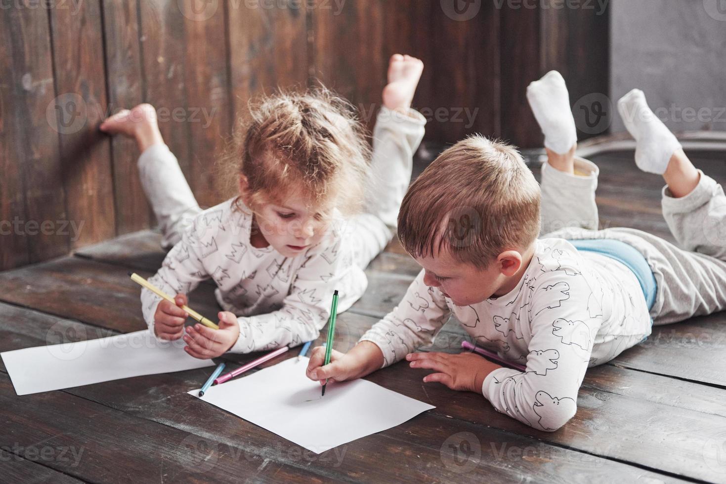 crianças deitam-se no chão de pijama e desenham a lápis. criança fofa pintando a lápis foto