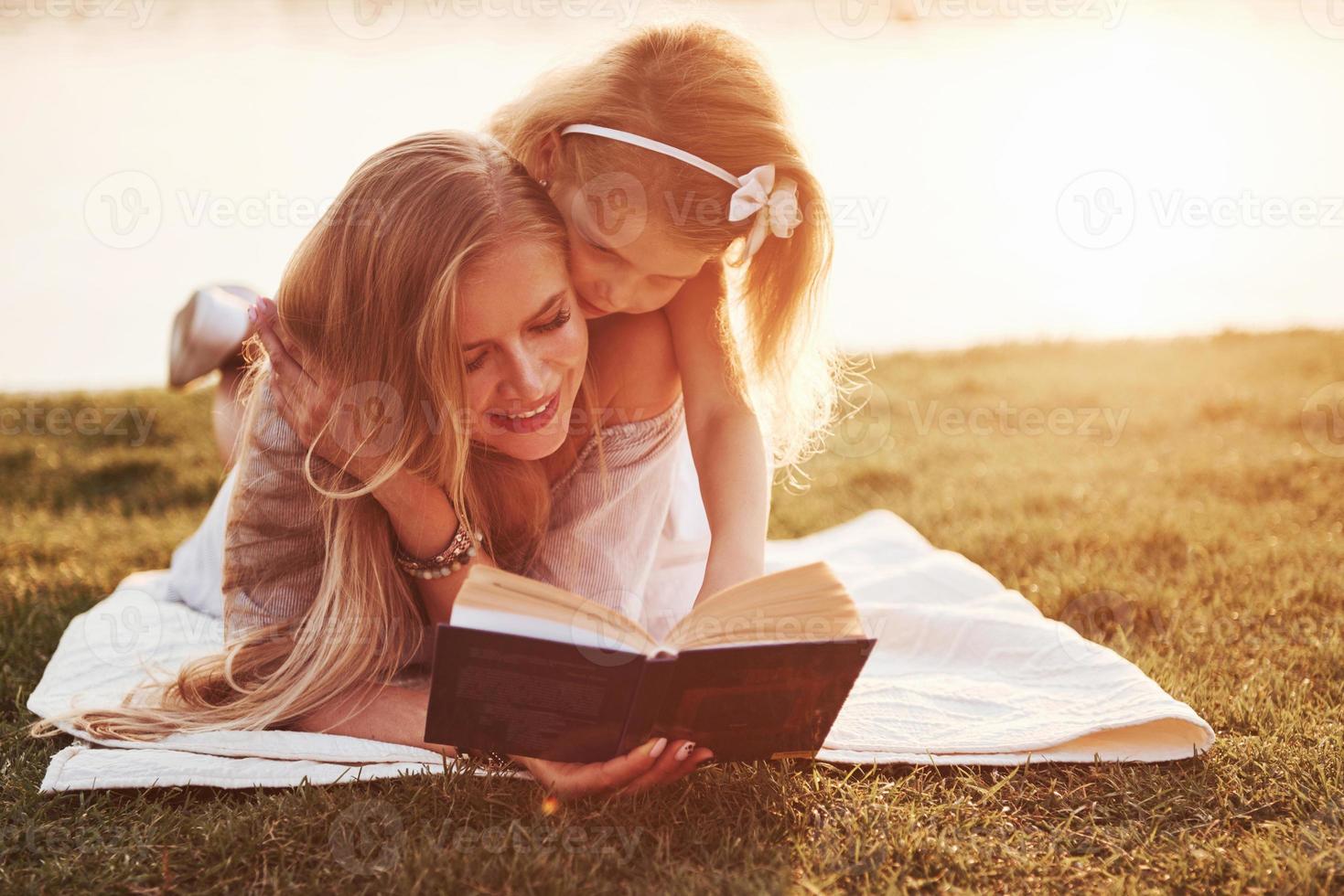 mãe com uma criança lendo um livro na grama foto