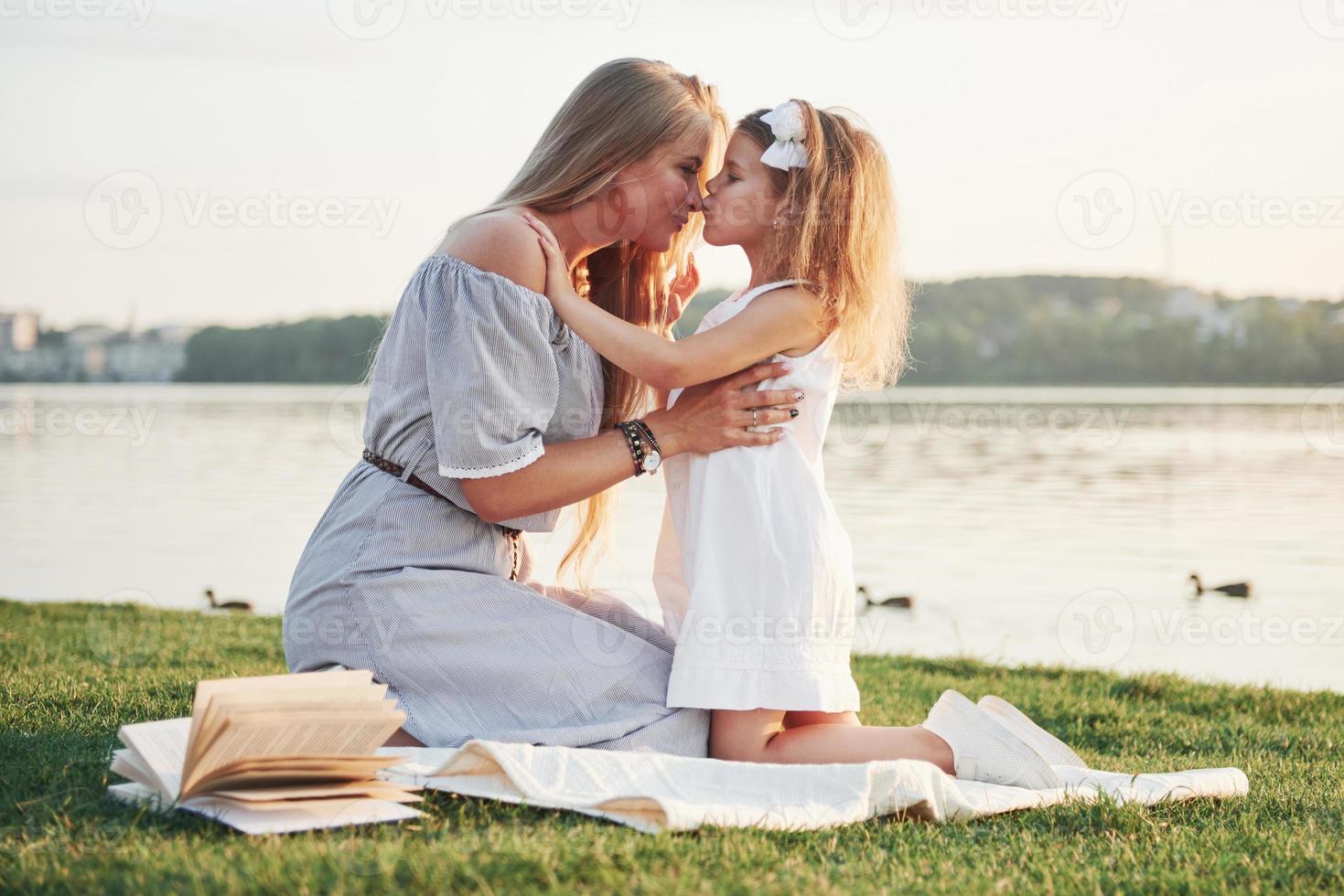 jovem mãe feliz com uma filha brincalhona em um parque perto da água foto