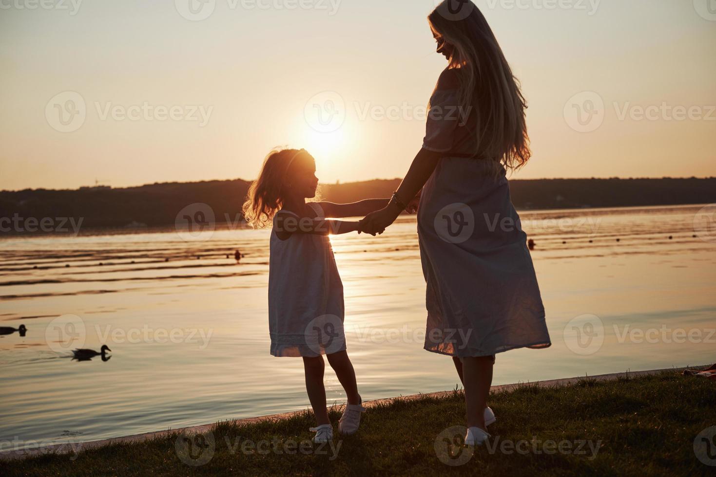 mãe brinca com seu bebê nas férias perto do mar, silhuetas ao pôr do sol foto