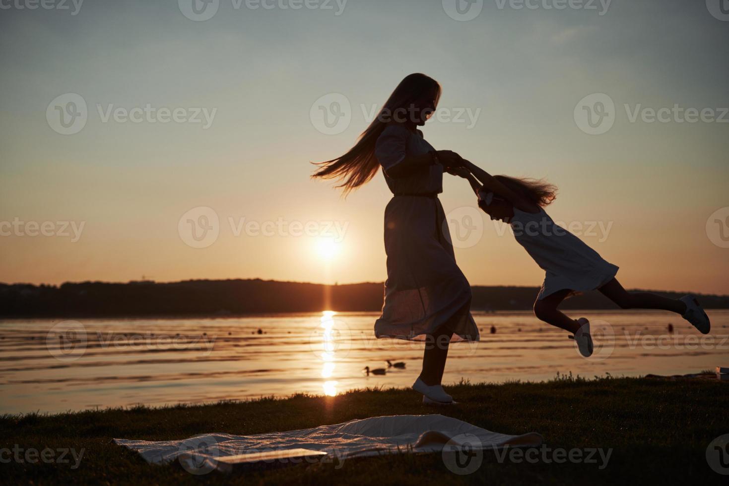 mãe brinca com seu bebê nas férias perto do mar, silhuetas ao pôr do sol foto