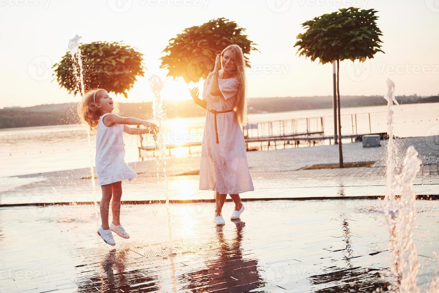 uma mulher brincando com uma criança perto do mar no parque ao pôr do sol foto