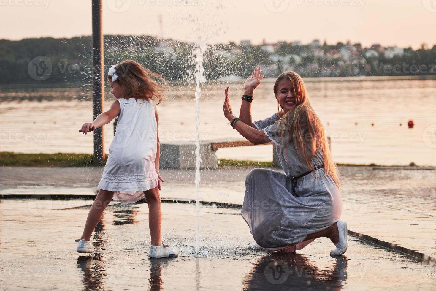 mãe com bebê perto da fonte ao pôr do sol foto